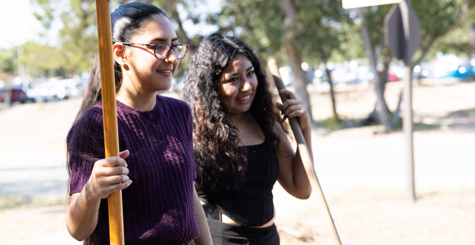 Two CTX students holding gardening tools smile as they serve in the environmental stewardship planting party